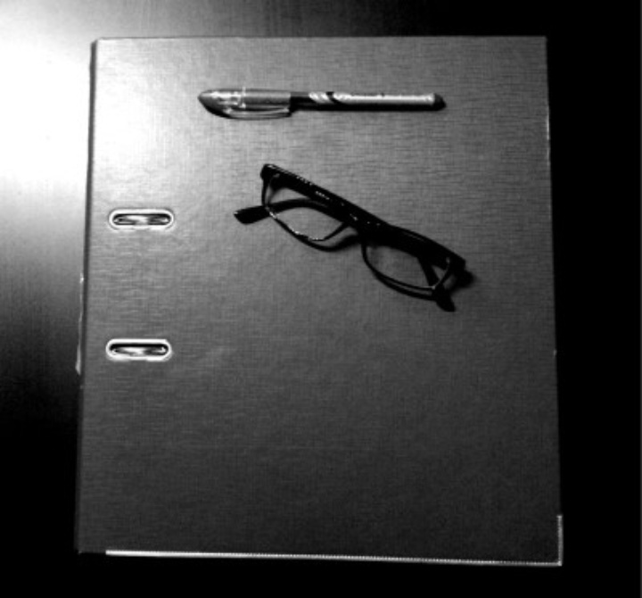 Auf einem Tisch liegt ein geschlossener Ordner. Auf dem Ordner liegen ein Stift und eine Brille.