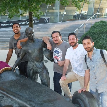 Eine Gruppe junger Männer aus dem Freundeskreis Flüchtlinge steht vor dem Mercedes Benz Museum. Sie lächeln in die Kamera.