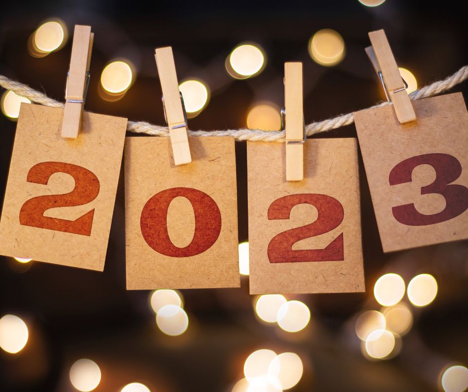Kärtchen mit Ziffern hängen an einer Wäscheleine - die Ziffern bilden die Jahreszahl 2023. Im Hintergrund Leuchtkegel von Lichterketten oder Kerzen.