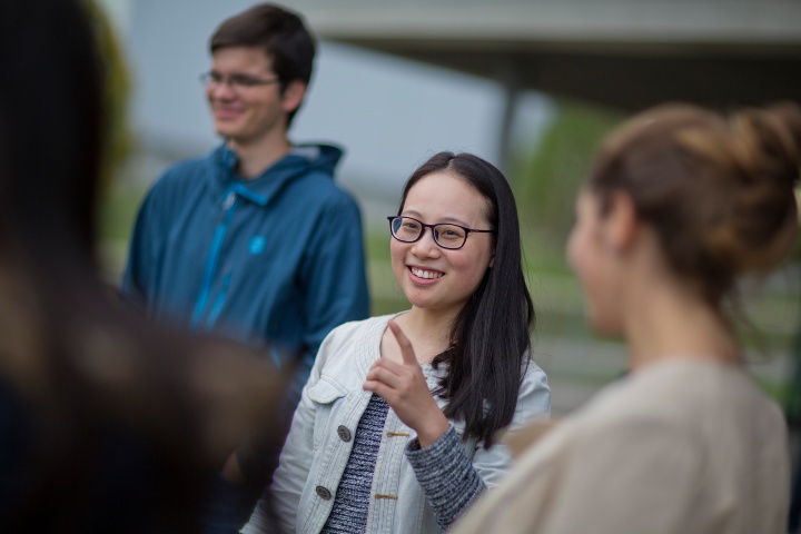 Eine Gruppe von Studierenden unterhält sich. Der Fokus liegt auf einer jungen Studierenden, die Personen um sie herum sind in unscharfen Umrissen zu sehen.