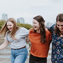 Drei Freundinnen laufen lachend Arm in Arm