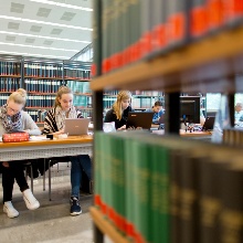 Studierende sitzen an Lernplätzen zwischen Bücherregalen in der Universitätsbibliothek zum Lernen.