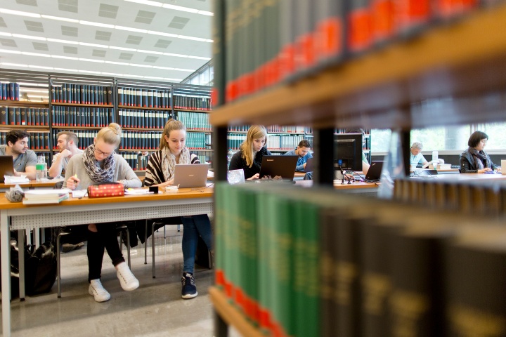 Studierende sitzen an Lernplätzen zwischen Bücherregalen in der Universitätsbibliothek zum Lernen.
