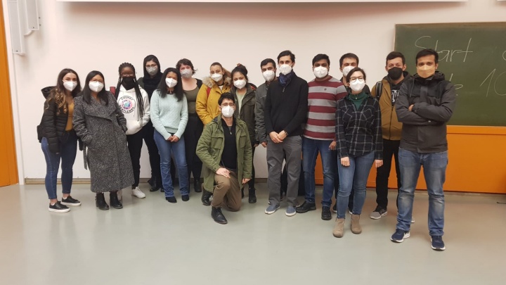 A group of students pose in front of a blackboard for a group photo. The people are wearing face masks.