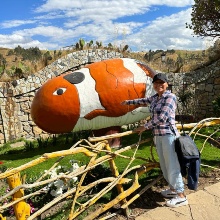 Lizbeth visits the Wanka Identity Park in Huancayo, Peru. She poses for a photo in front of a statue representing an anomen fish in the colors white and orange.