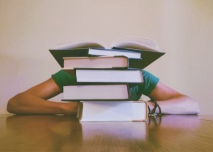 Symbolic image: A person sits at a table behind a stack of books. You can only see her elbows.