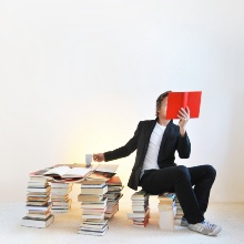 Person sits on stacks of books and reads a book