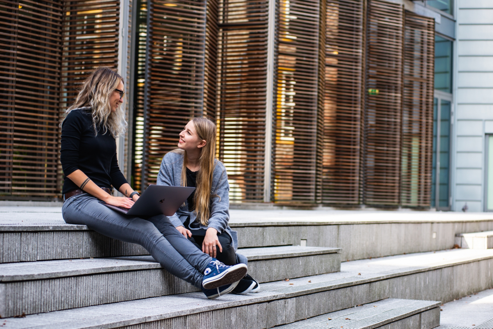 Zwei Studentinnen sitzen auf einer Treppe und unterhalten sich
