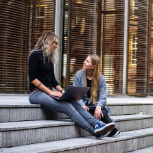 Zwei Studentinnen sitzen auf einer Treppe und unterhalten sich